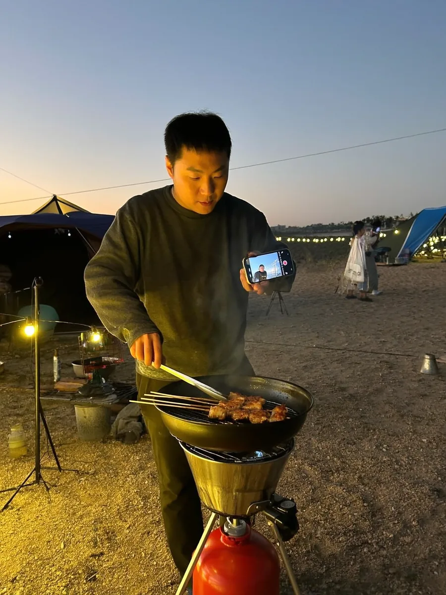 캠핑장에서 꼬치를 구우며 촬영하는 크리에이터